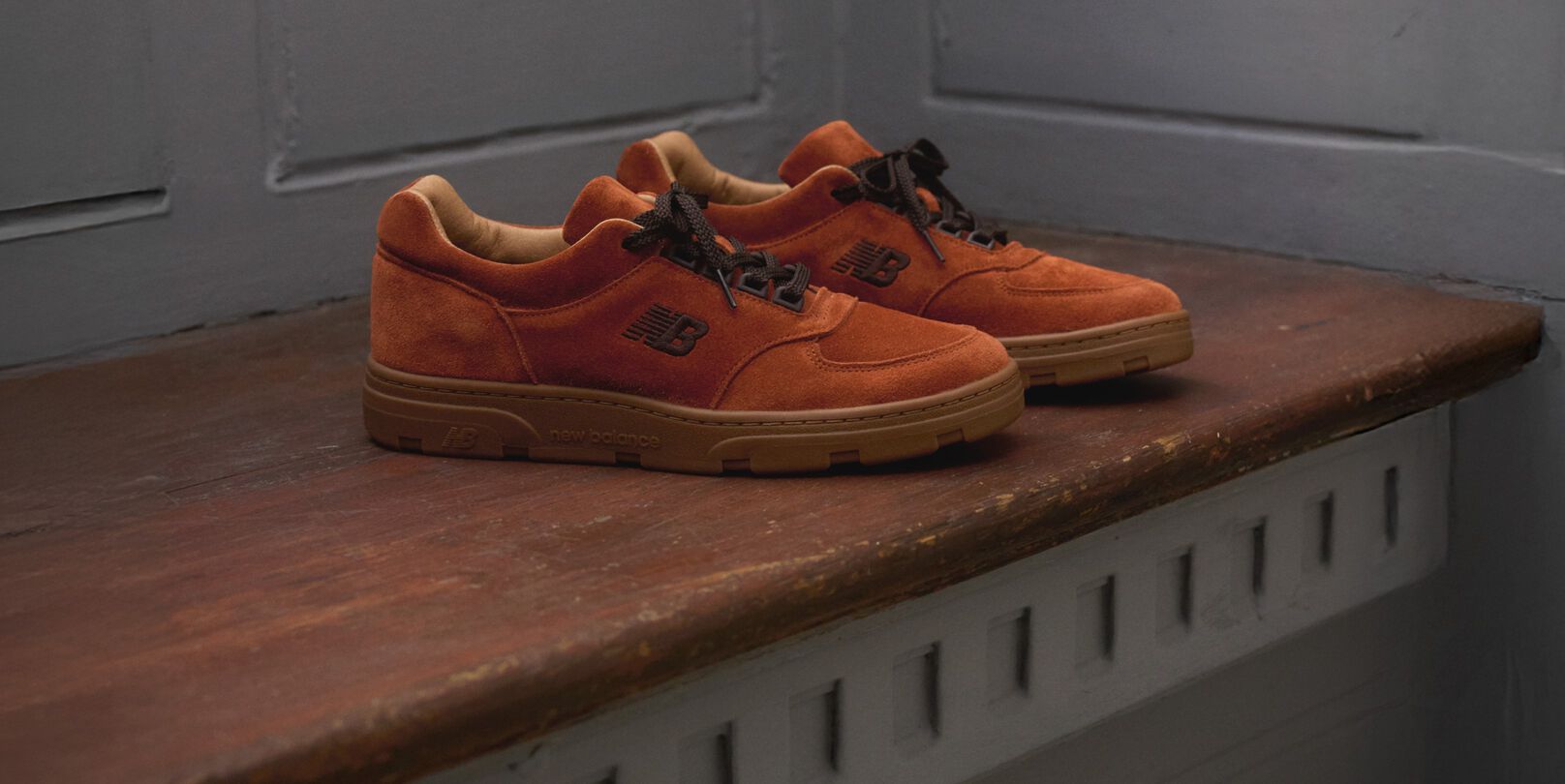 A pair of New Balance Made in UK sneakers sitting on a wooden window seat with panel detailing on the walls.